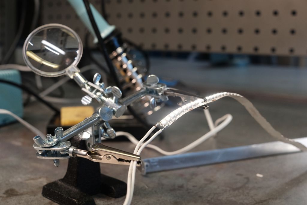 Stativ med to klemmer som holder fast ledninger og ei LED-stripe. Foto.