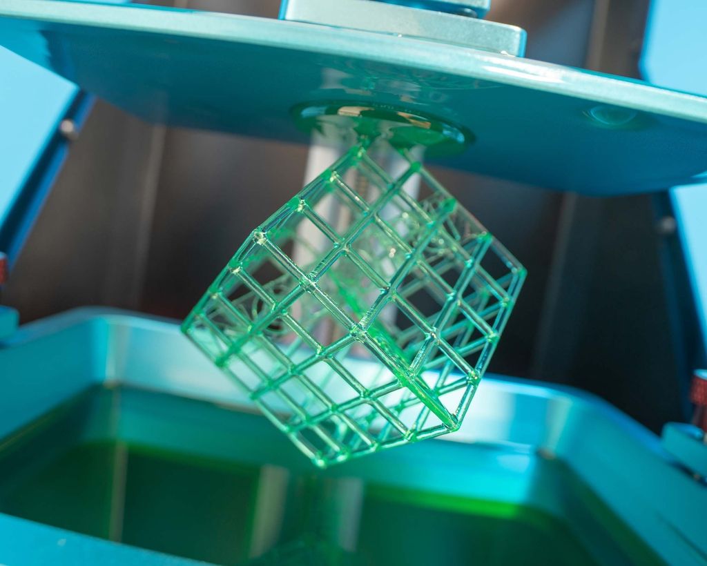 Kube med gittervegger hengende på en 3D-printer. Foto.
