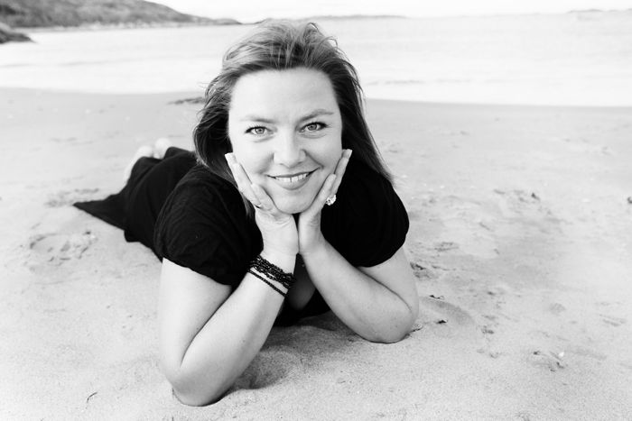 Ei dame ligg med hovudet i hendene på ei strand. Ho ligg rett mot kameraet slik at vi opplever ei forkorting av kroppen. Foto.