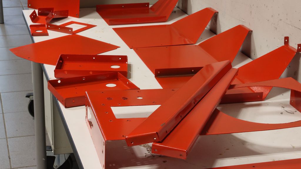 Et stort antall små og store metalldeler i ulike fasonger liggende på et bord. Delene er ferdig knekt og pulverlakkert. Foto