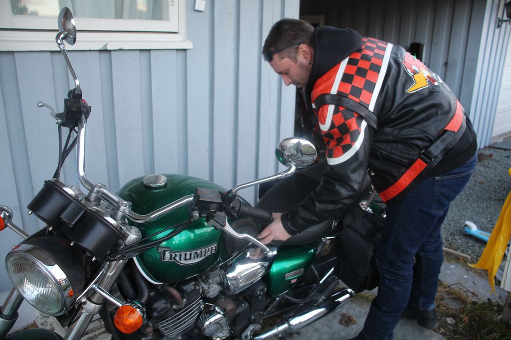 Foto av en mann med motorsykkeljakke som fester setet på en grønn motorsykkel. 