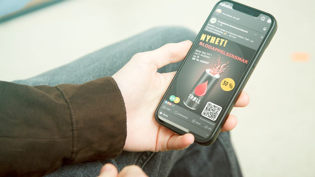 En person som holder en mobiltelefon som viser et innlegg på Facebook fra Kongsland mineralvannfabrikk om den nye drikken Trøll. Foto.