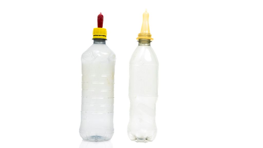 To halvliters brusflasker med hver sin tåtesmokk. Den ene smokken er festet til en skrukork, mens den andre er tredd ned over flasketuten. Foto.