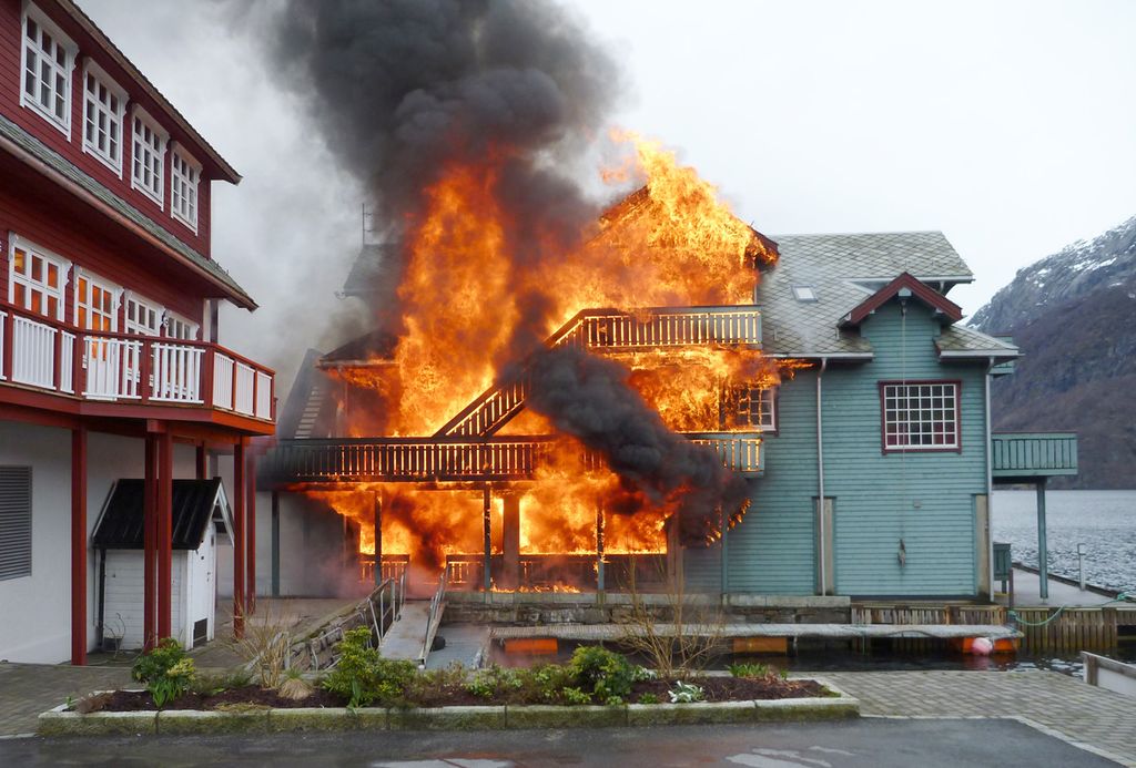 Et hus står i full brann. Det er andre hus i nærheten, og huset ligger helt til sjøen. Foto.