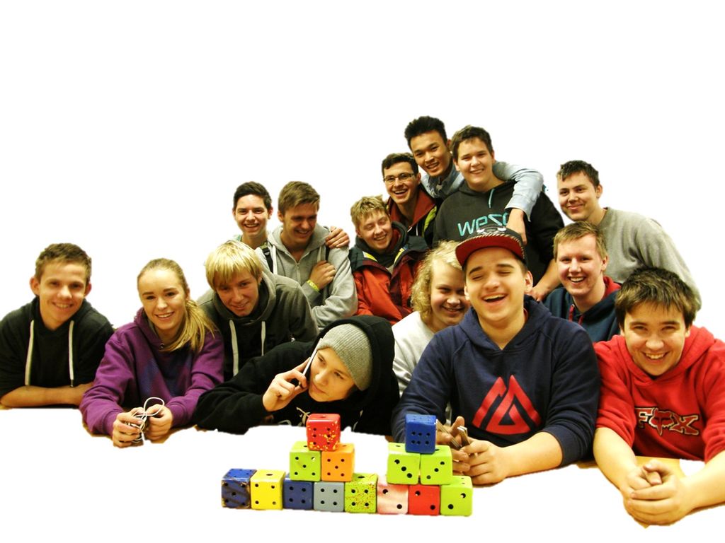 14 gutter og éi jente foran et bord med fargerike terninger. Foto.