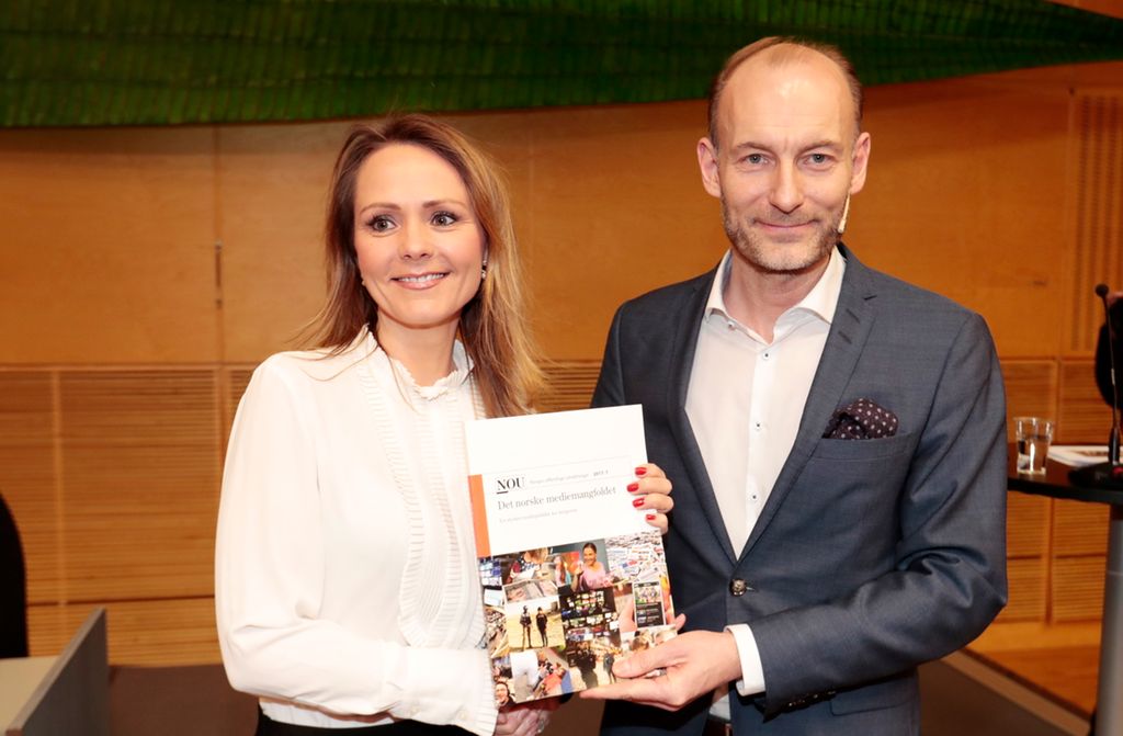 Foto av en kvinne i hvit bluse og en mann grå i dress som viser fram en skriftlig rapport.