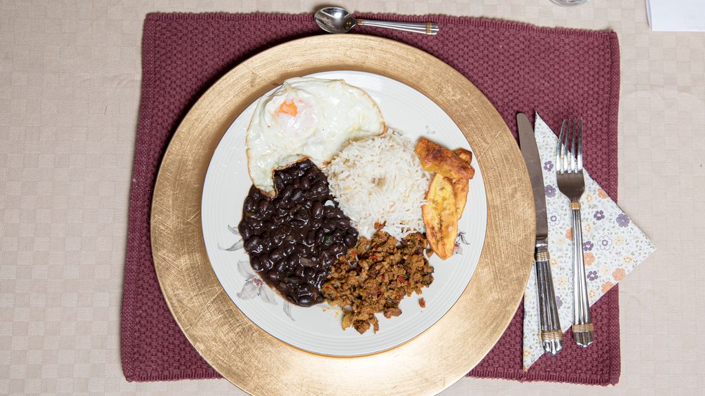 En tallerken med den venezuelanske matretten pabellón criollo, bestående av ris, stekte bananskiver, kjøttdeig, sorte bønner og et speilegg. Foto.