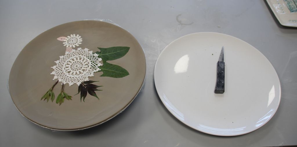 Et fat, kniv og  leire med blonder og planter som danner fugledekor. Foto.