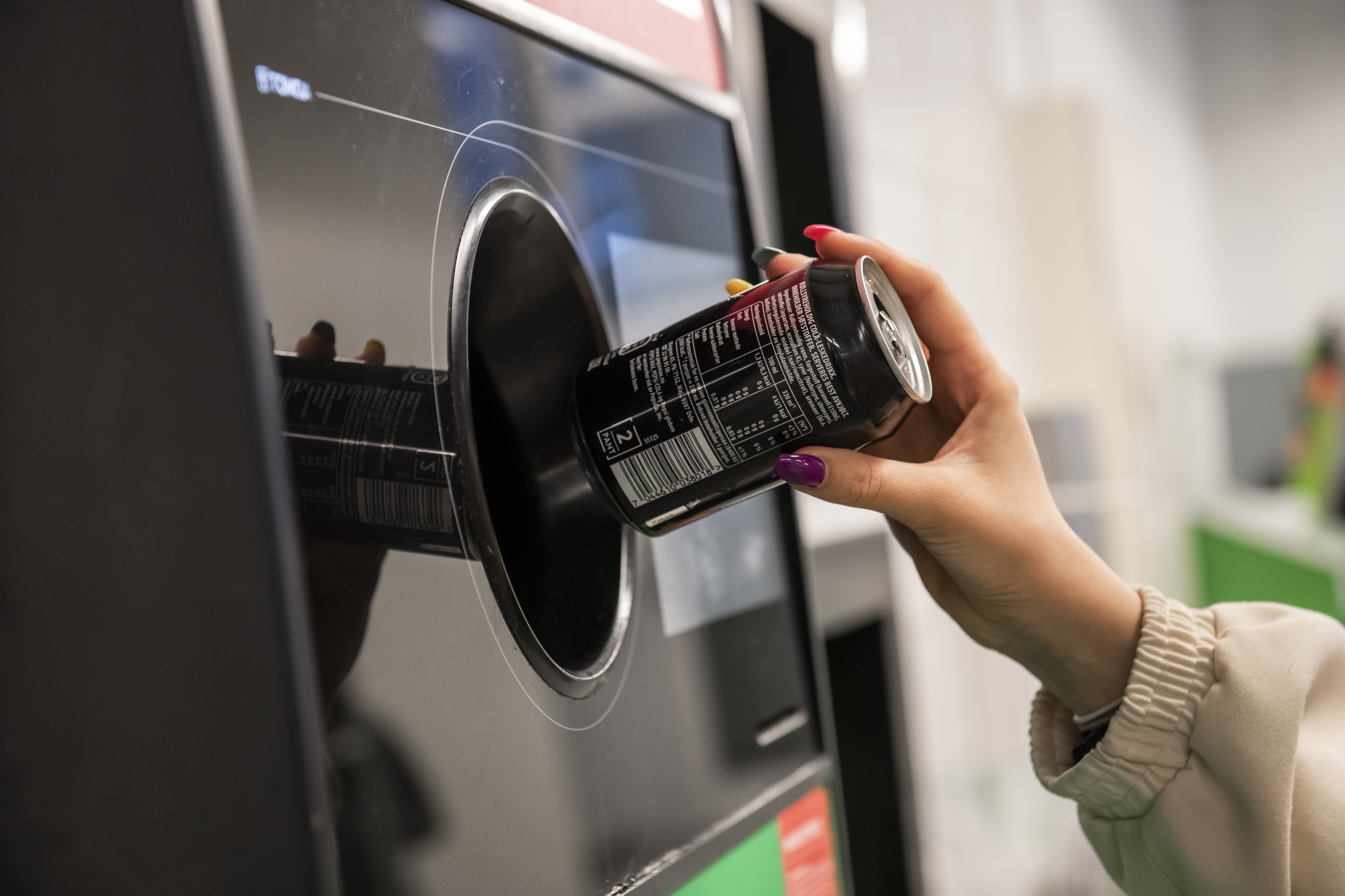 Ei hand er i ferd med å sleppe ein brusboks inn i ein panteautomat. Foto. 