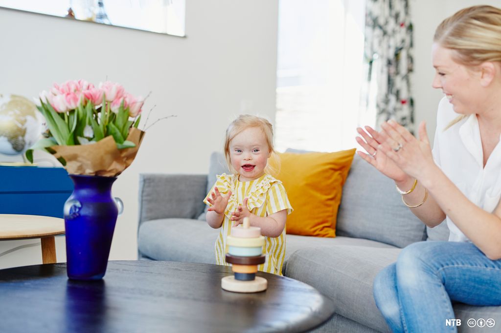 Ei lita jente klapper i hendene sammen med en voksen. Foto.