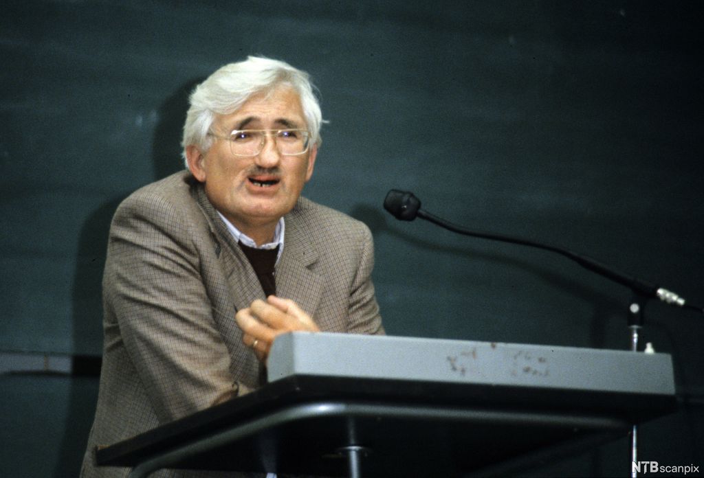 Mann med grått hår og bart held foredrag. Foto.