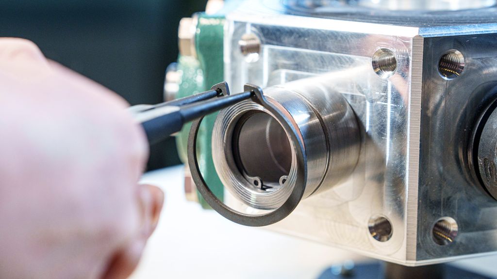 Ei tang festa i hull på endene av en ring. Tanga utvider ringen, og den er på vei inn på en aksling hvor det er frest et spor et stykke inn. Foto.