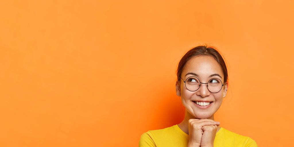 En ung kvinne smiler mot oransje bakgrunn. Foto.