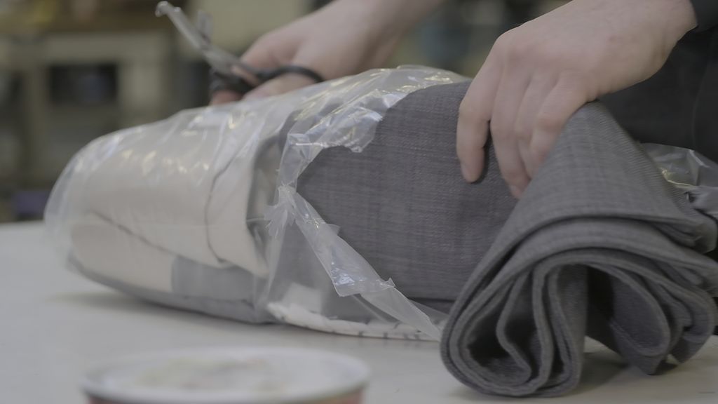 Person tar grå tekstiler ut av en pose. Foto.