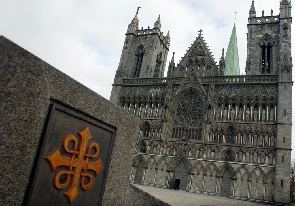Fronten av ei stor domkirke. På muren i forgrunnen er pilegrimsledens emblem. Foto.