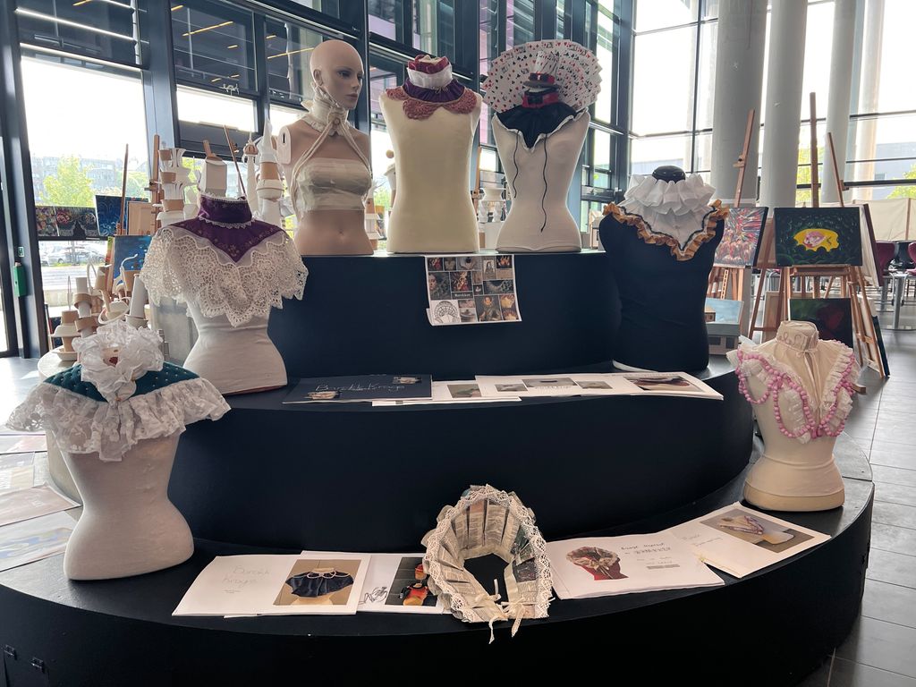 Sju utstillingsdukker har barokke krager og er utstilt på et podium sammen med prosesshefter. Foto.