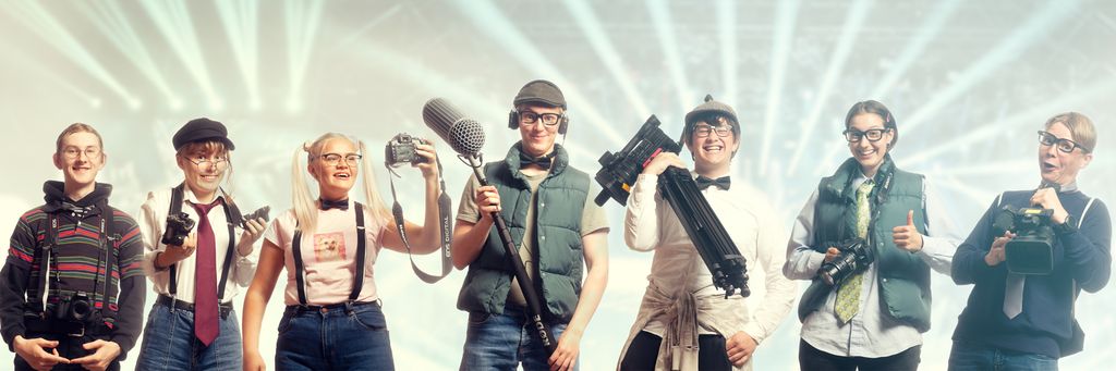 Ei gruppe ungdommar har kledd seg ut med nerdete klede og står oppstilt på rekkje med forskjellig utstyr for medieproduksjon. Foto.