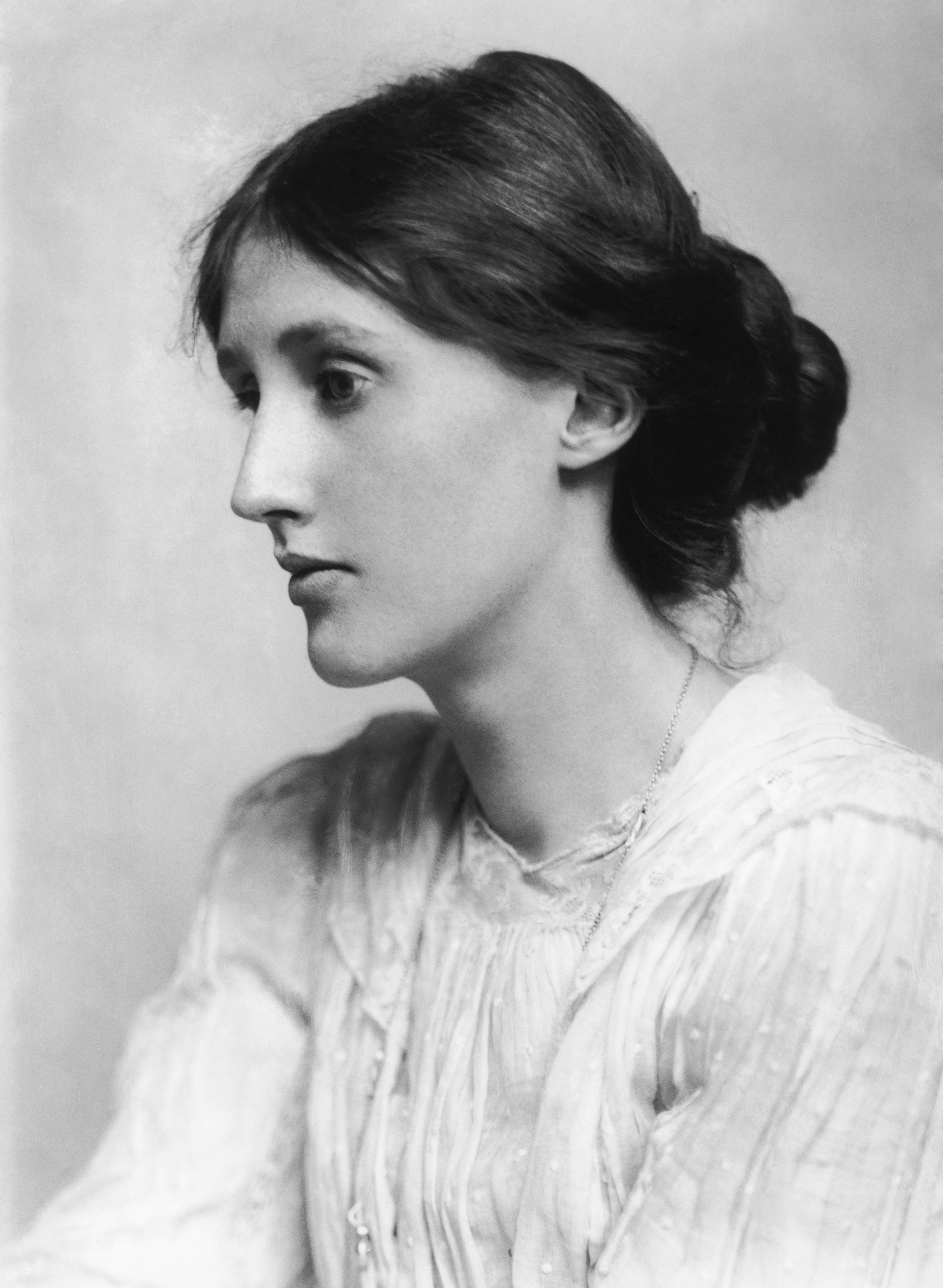 Photo: Portrait of a young woman. She has dark hair, gathered in a bun at the back. She has a serious expression. She is wearing a white blouse. 