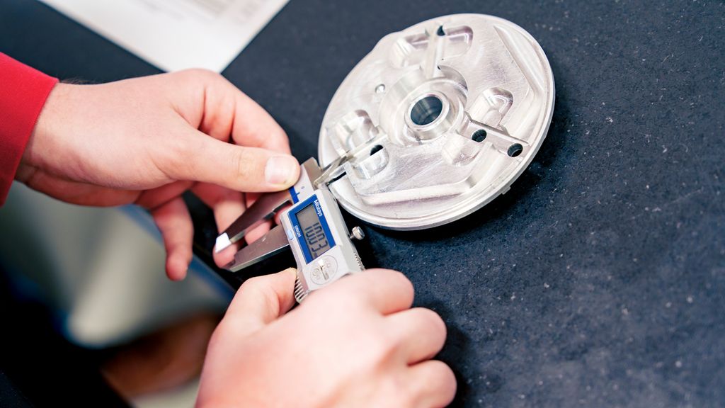 En person måler med et digitalt måleverktøy på en sølvfarga, rund gjenstand. Foto.