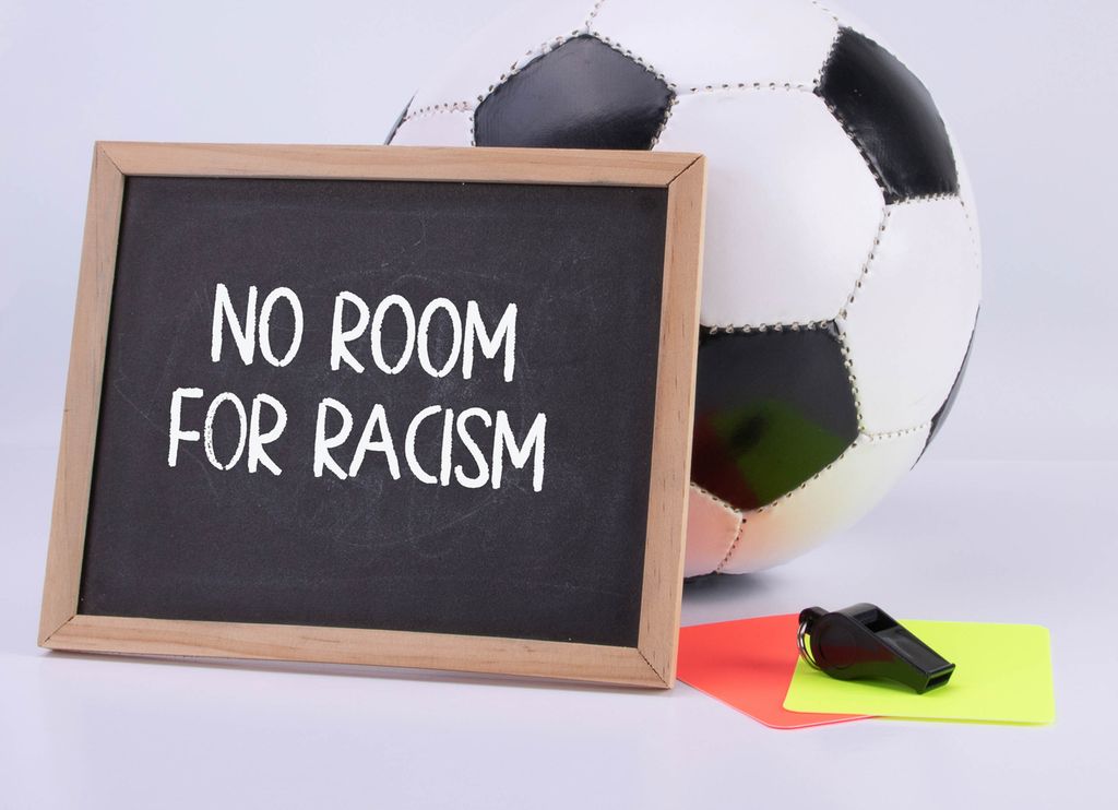 Tavle med teksten "No room for racism" lent opp mot en forball. Foto.