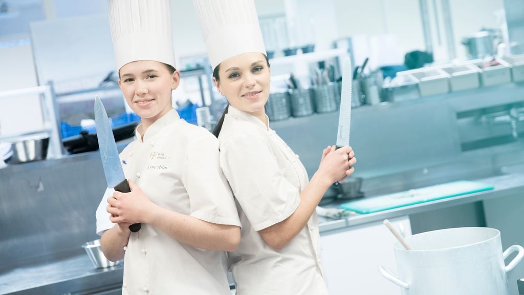 To kokker står rygg mot rygg med store kjøkkenkniver. Foto.