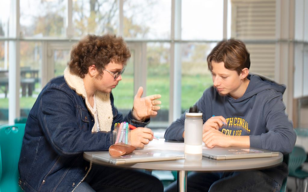To gutter sitter i en kantine og diskuterer. Foto.