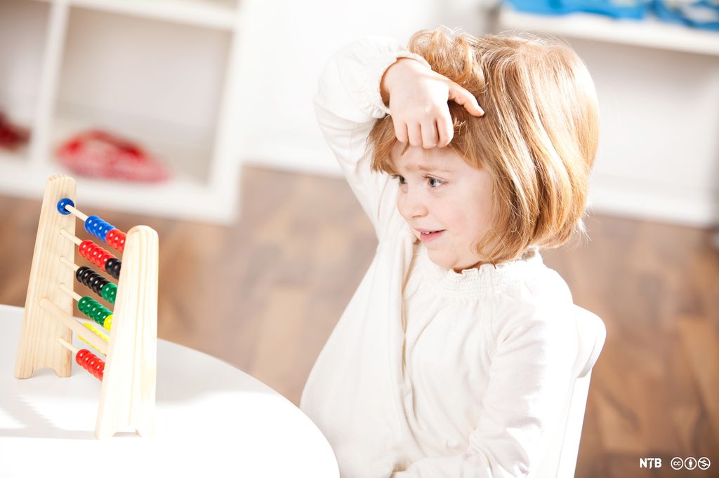 Et barn ser på ei kuleramme. Hun holder den ene hånden på hodet. Foto. 