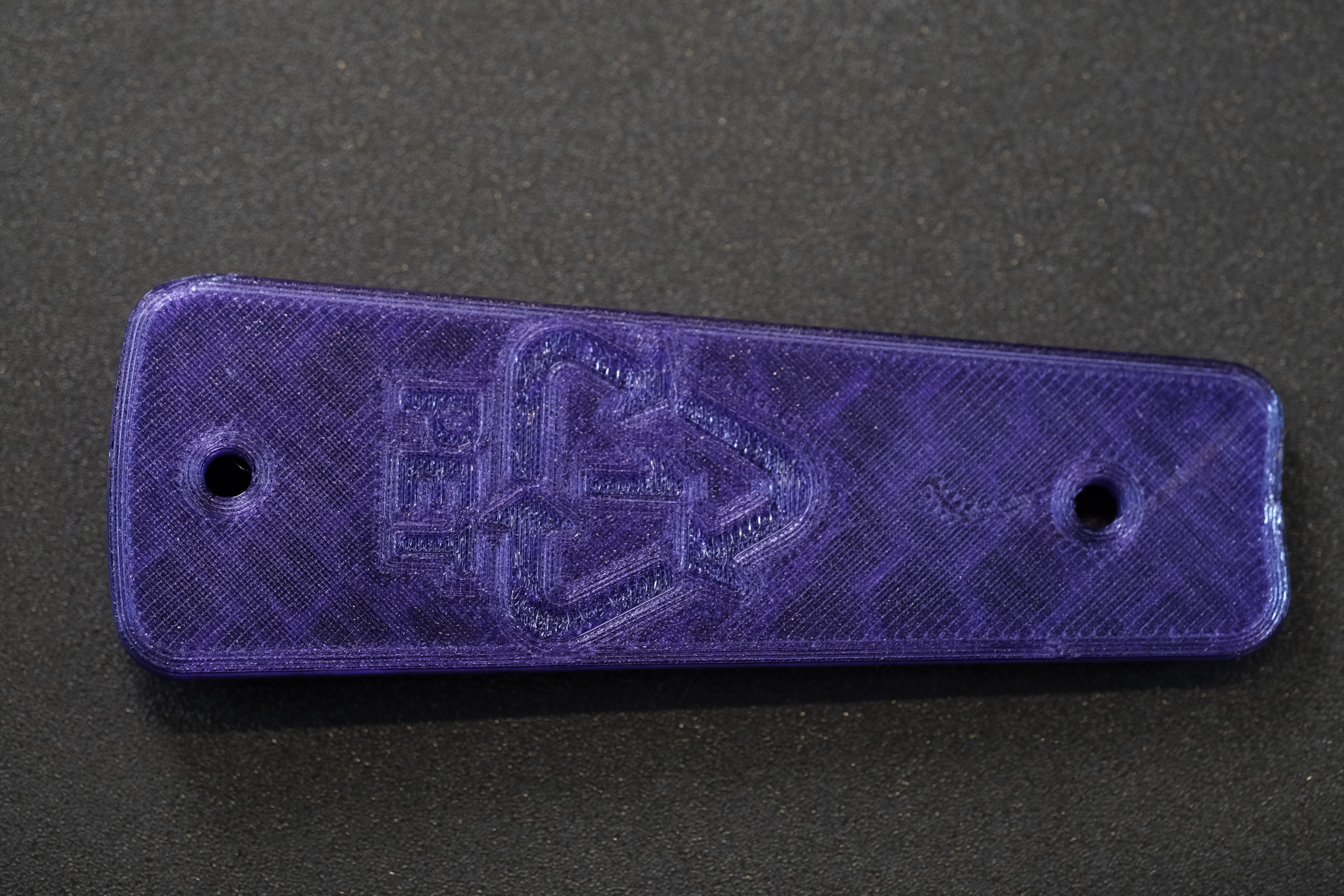 Nærbilete av baksida av eit lilla rekkerthandtak. Resirkuleringssymbolet for PET er printa inn midt på. Foto.