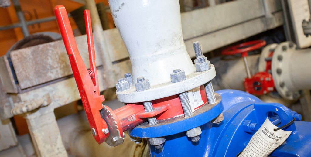 En manuell dreiespjeldventil som er montert med boltet flens på inngangen til en sentrifugalpumpe. Ventilen er rød, og pumpen er blå. Ventilen står i åpen posisjon. Foto.