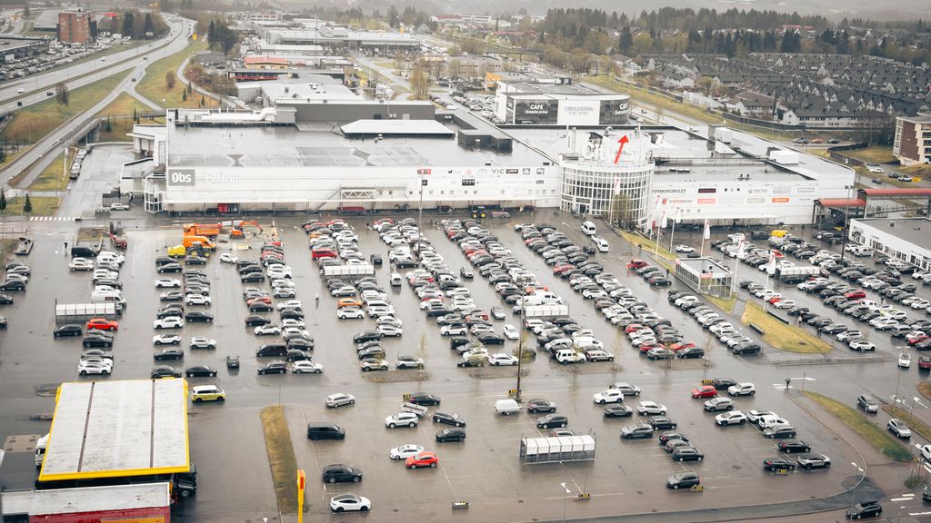 Stor parkeringsplass med mange biler foran et stort kjøpesenter. Bildet er tatt fra lufta. Foto. 