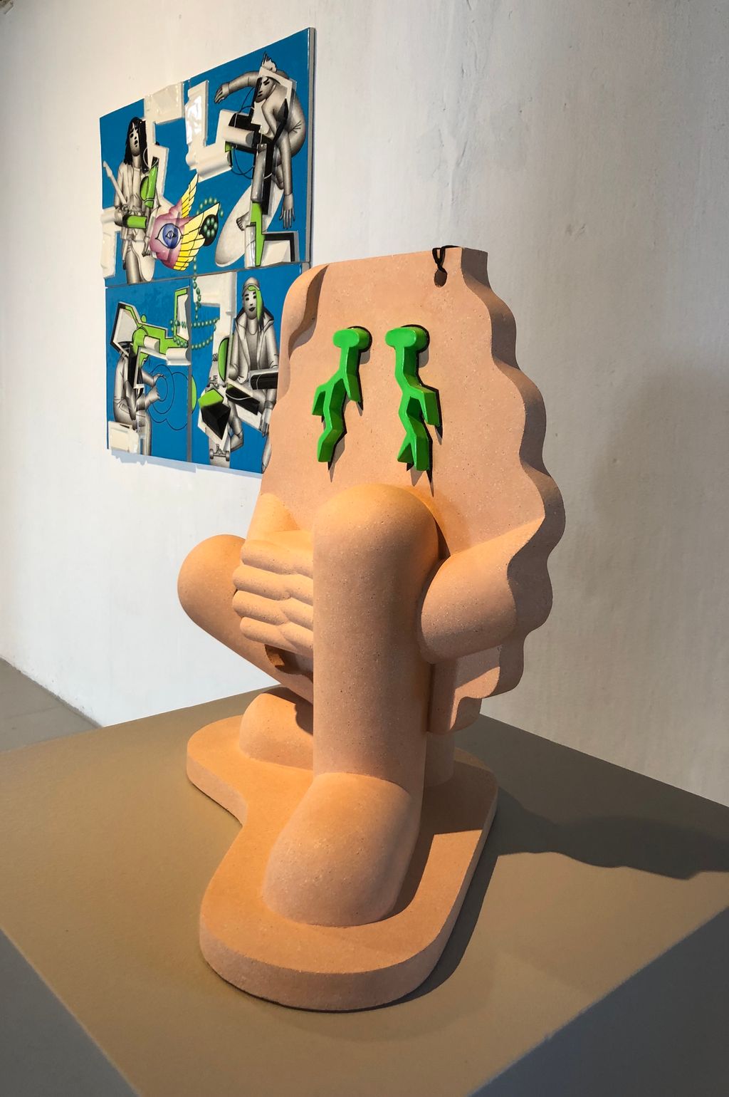 Keramikkskulptur framom eit relieff som er laga i steingods, måla med porselensmåling. Foto.