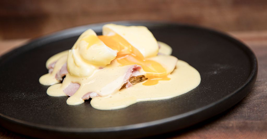 Egg benedict på en svart tallerken. Foto.