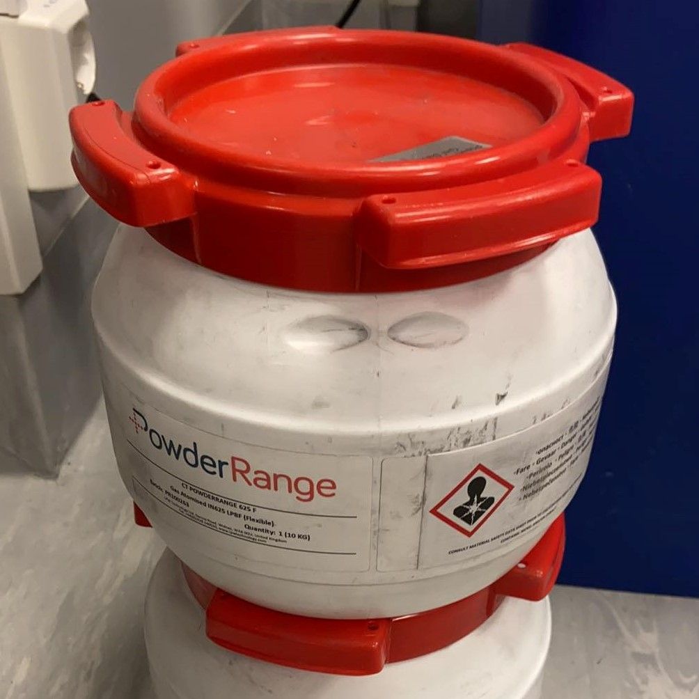 En hvit, rund beholder med rødt lokk og rød bunn som inneholder metallpulver. Foto.