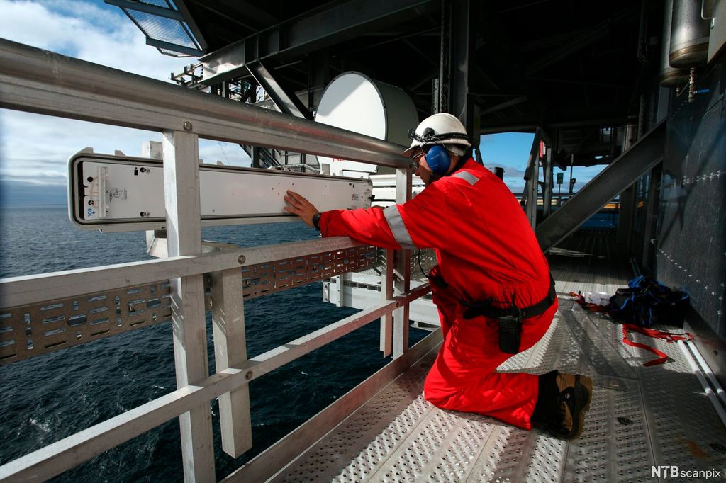 En elektriker monterer en lysarmatur på en oljeplattform. Foto.