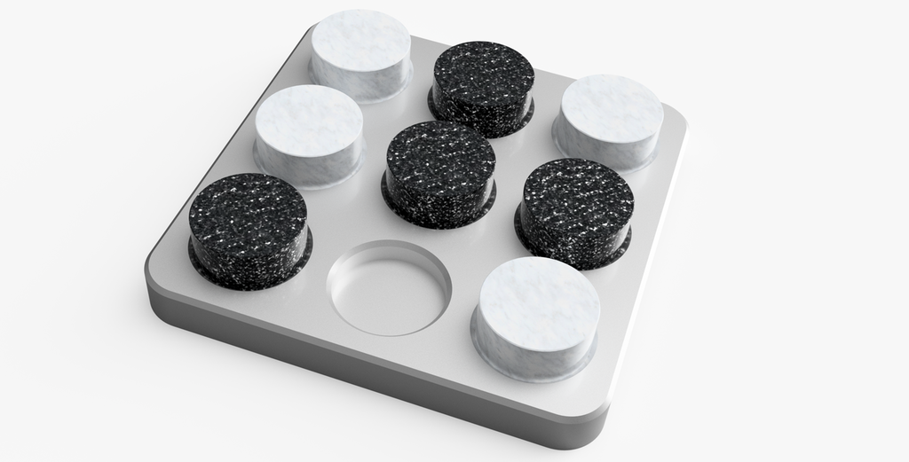 Kvadratisk spillebrett for tre-på-rad-spill. Brettet er lagd av aluminium og har avrunda kanter. Det er ni fordypninger å plassere spillebrikker i. Fire hvite og fire svarte spillebrikker av marmor er plassert på brettet. Foto.