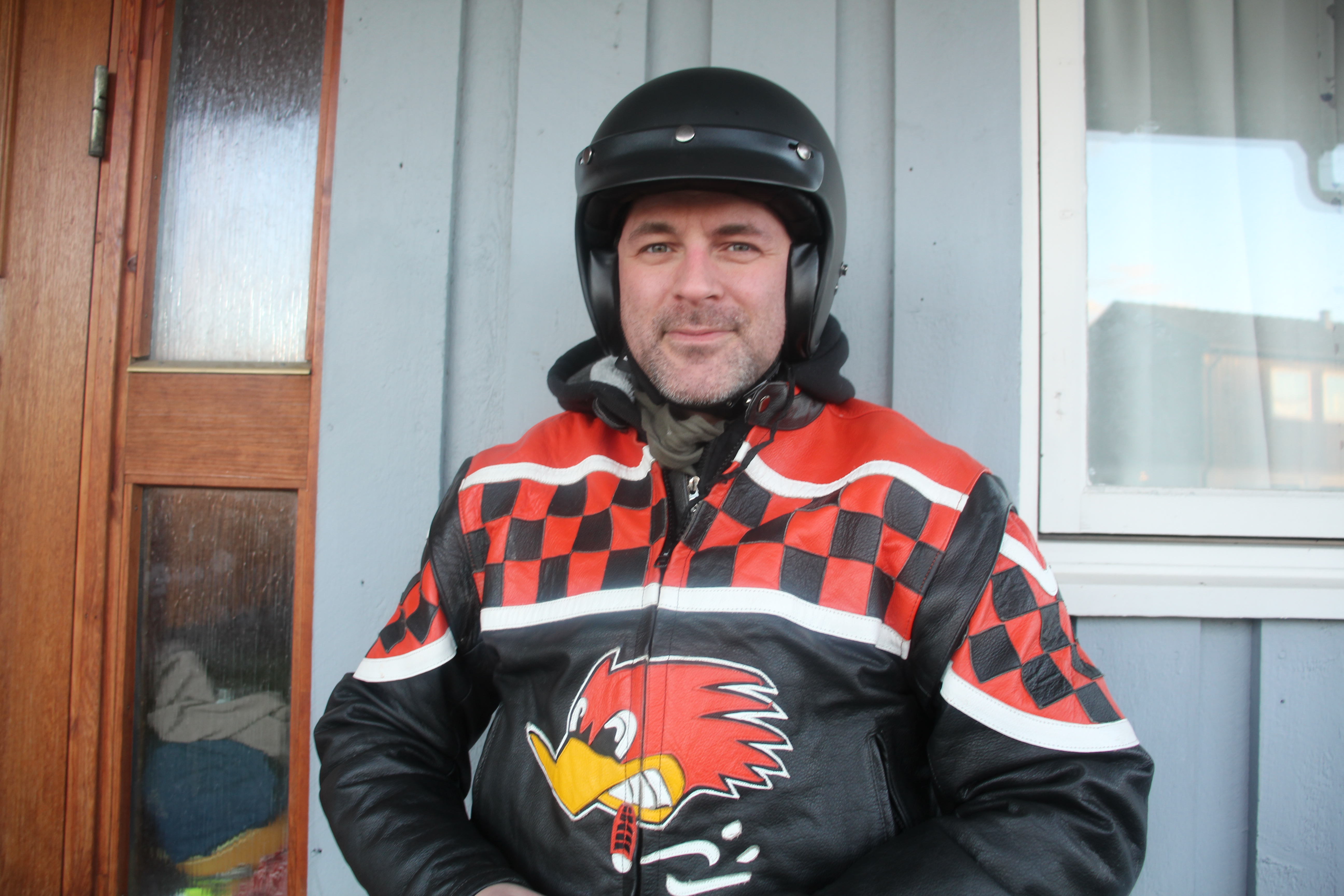Foto av mann med fargerik motorsykkeljakke og svart halvhjelm.