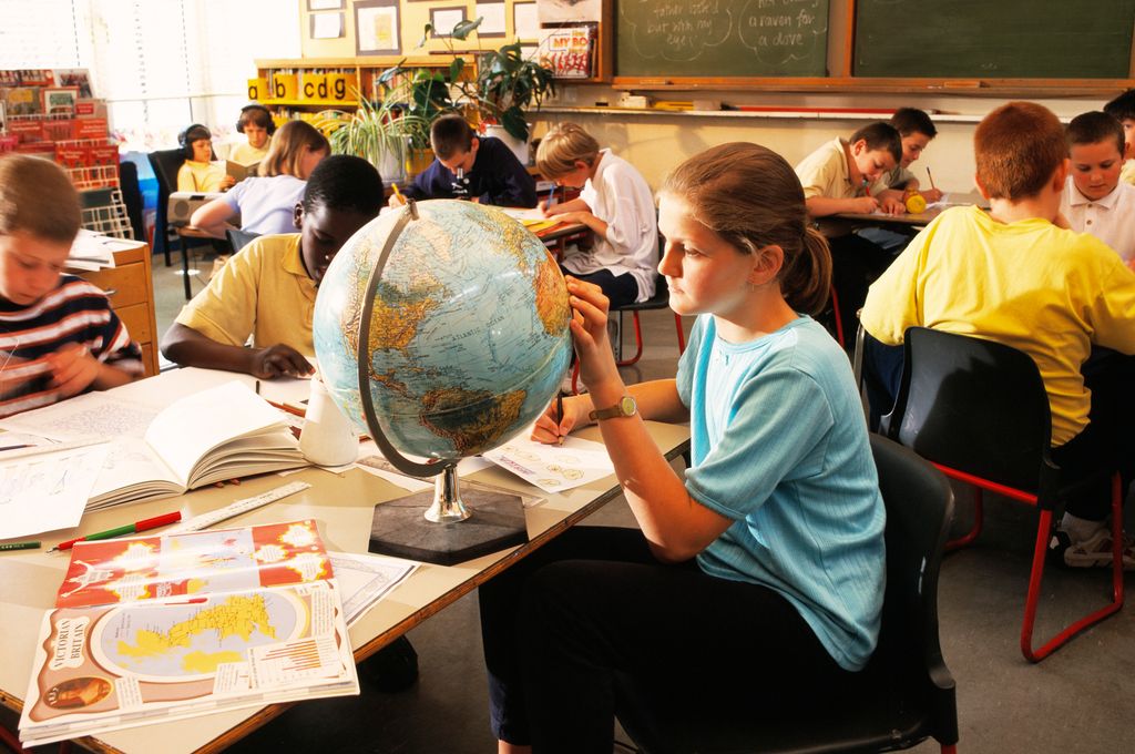 Schoolgirl looking at Africa on a globe. A book (lower left) is open at pages about Victorian Britain and the British Empire. Photo.
