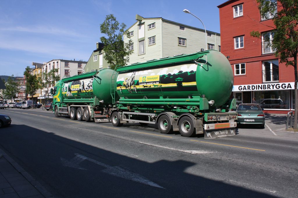 En stor Felleskjøpet-lastebil med henger kjører gjennom ei bygate. Foto.