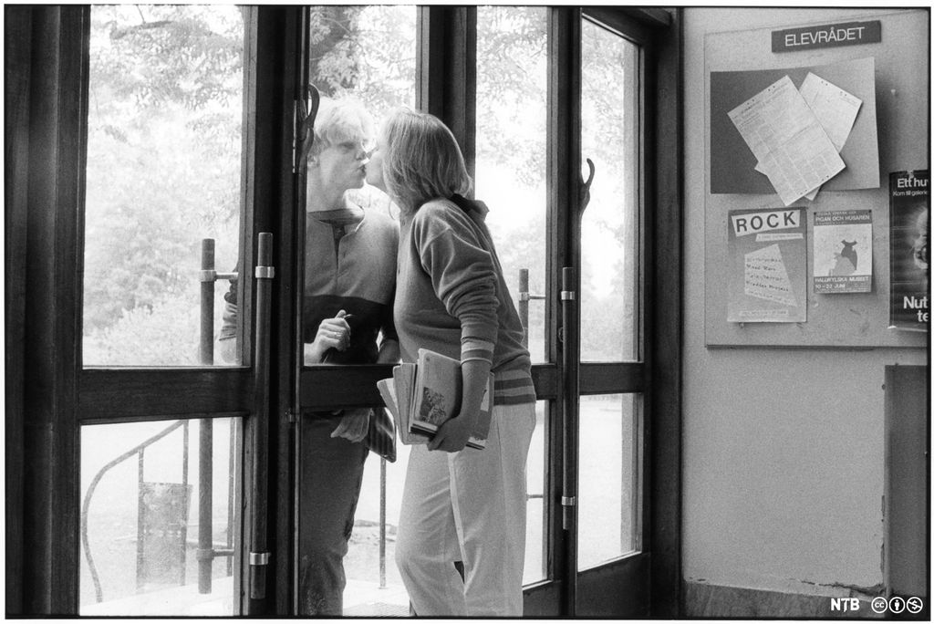 To ungdommer kysser hverandre med en glassdør imellom seg. Foto.