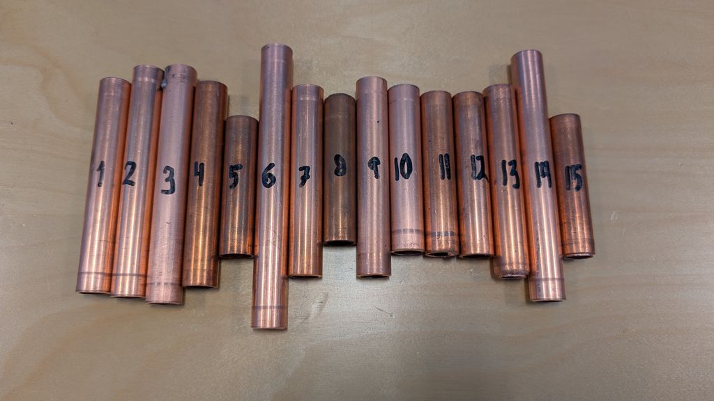 15 nummerte stubbar av koparrøyr har ulike lengder og ligg ved sida av kvarandre. Dei er ikkje sorterte etter lengde. Foto.