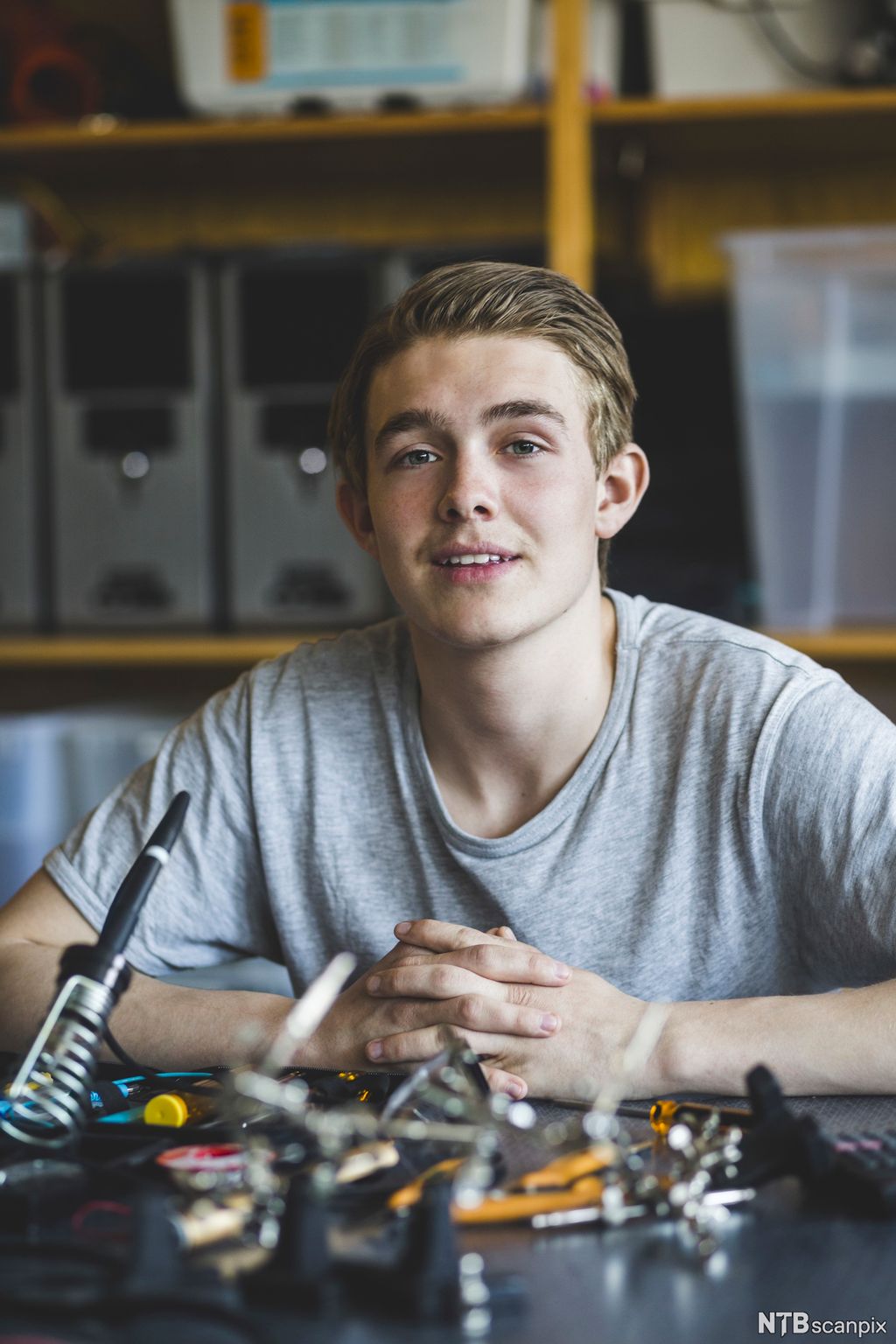 Gutt sitter ved bord med verktøy og utstyr til forsøk. Foto.