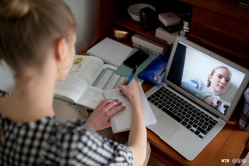 Ei jente tar notater mens hun snakker med ei annen jente på videochat. Foto.