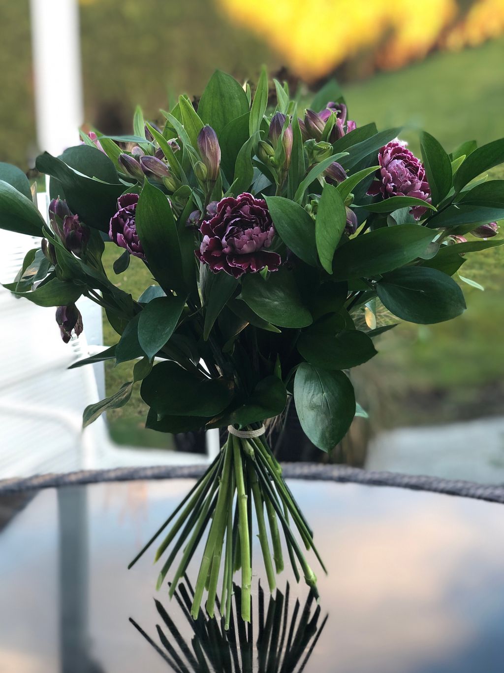 En bukett lilla blomster med glatte grønne blader står på et bord. To tredjedeler av buketten er over bindepunktet, den siste tredjedelen under. Foto. 