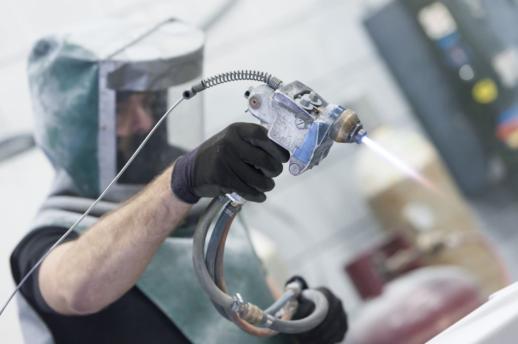 Arbeider i verneutstyr holder på med plasmabehandling av metalloverflate. Foto.