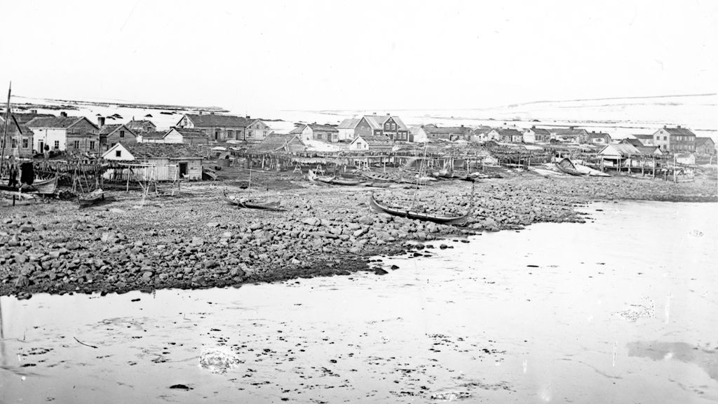 Busetnad ved sjøen. Busetnaden er prega av trehus, nokre med ein etasje og nokre med to etasjar. Svart-kvitt foto.