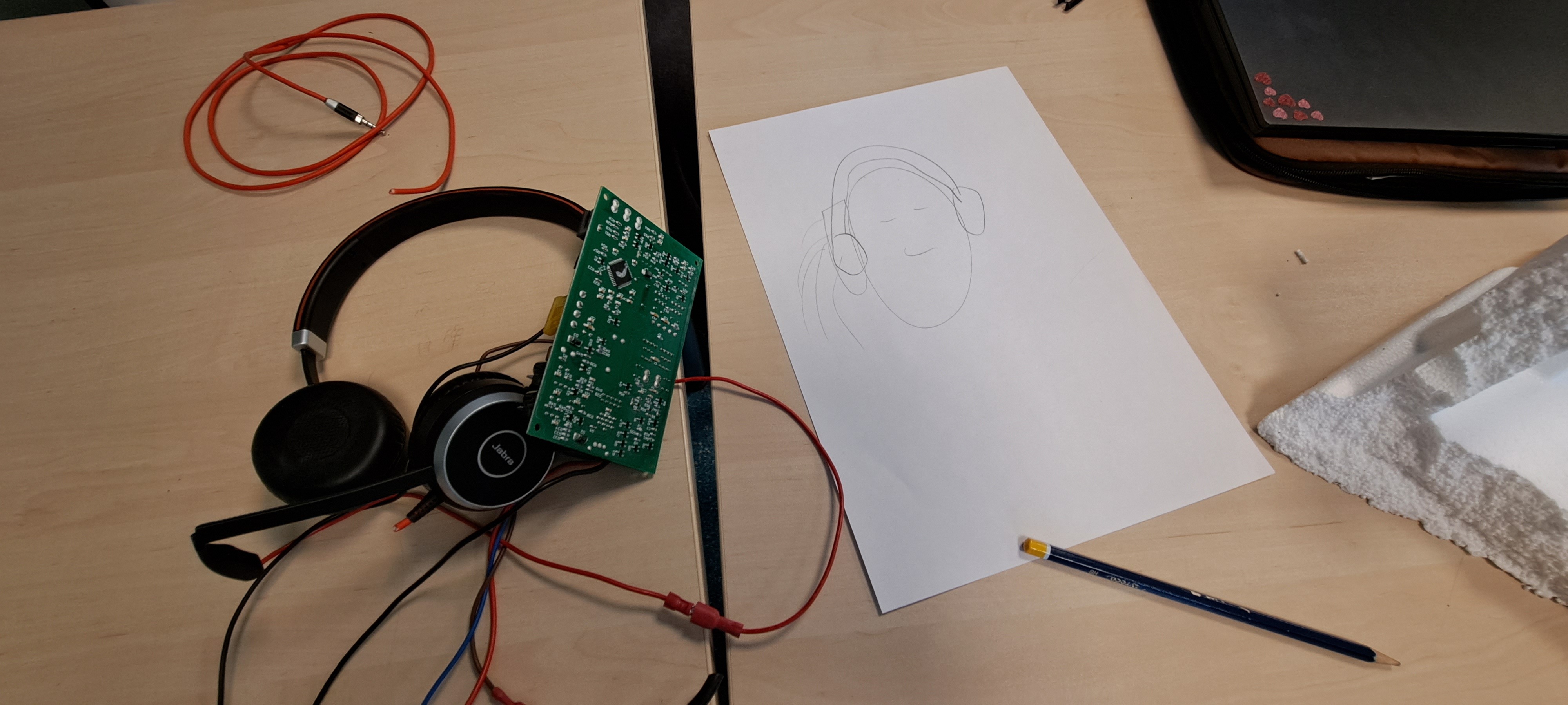 Hodetelefoner med ledninger og kretskort ved siden av en tegning av en person med hodetelefoner. Foto.