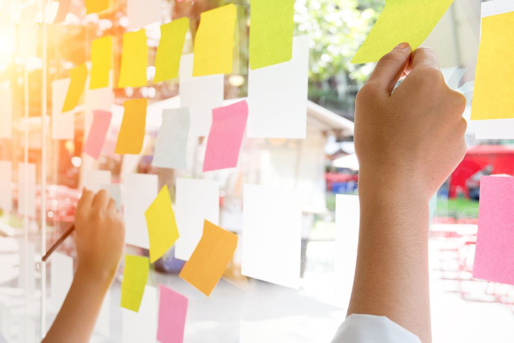 Hender som skriver på post-it lapper på et vindu. Foto.