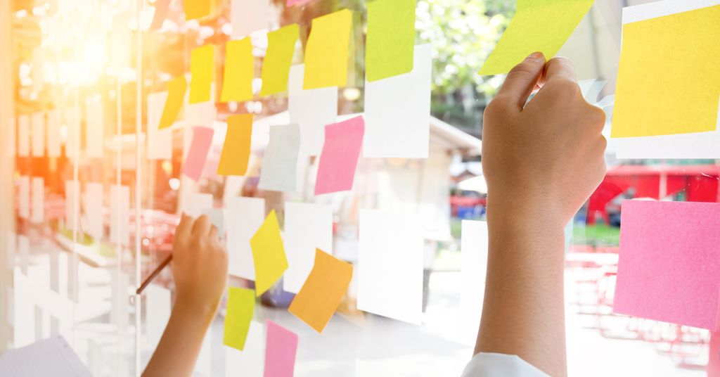 Hender som skriver på klistrelapper på en vegg. Foto.