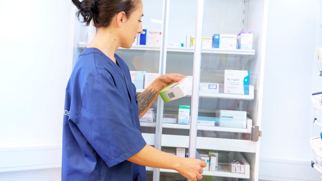 Apotektekniker tar ut medisin fra et låsbart skap. Foto.