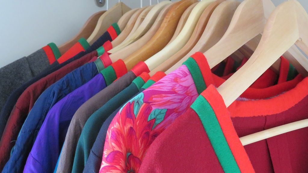 Utsnitt av kofter i ulike farger som henger i et skap. Foto.